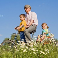 Kids riding with their grandfather on the daisies field againstr blue sky